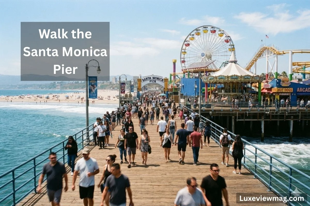 A scenic view of people walking along the Santa Monica Pier, with the ocean and amusement rides in the background.