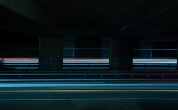 A long exposure photo Hitlmila trails beneath an overpass at night.