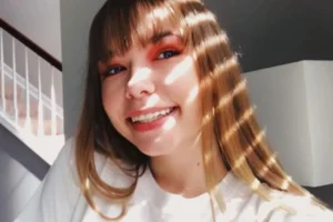 Whitney Mathers, a woman with long hair, dressed in a white shirt, exuding a sense of style and confidence.