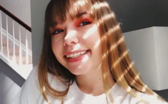 Whitney Mathers, a woman with long hair, dressed in a white shirt, exuding a sense of style and confidence.