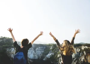 Two women raise their arms in the air, expressing excitement after realizing the traveler hired the wrong tour guide.