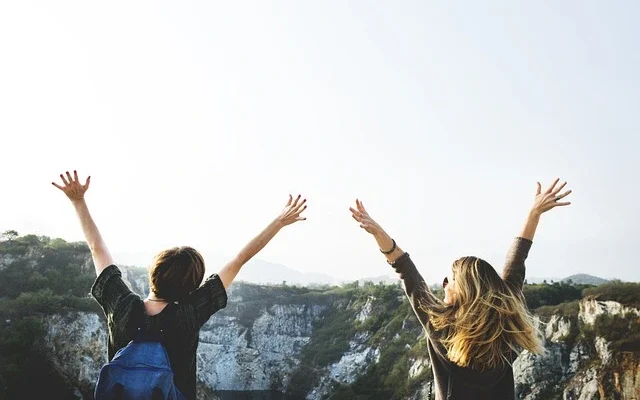 Two women raise their arms in the air, expressing excitement after realizing the traveler hired the wrong tour guide.