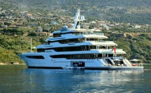 A large yacht, owned by arthur blank yacht, positioned in tranquil waters adjacent to a picturesque mountain landscape.