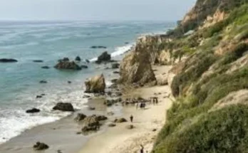 El Matador State Beach showcasing a rugged cliff beside the beach, with clear blue water lapping at the shore.