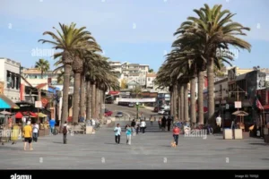 People stroll along Pier Avenue in Hermosa Beach, lined with palm trees and city scenery.