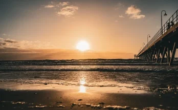 Sunset over a pier at Hermosa Beach, with the sun casting warm hues behind the structure.
