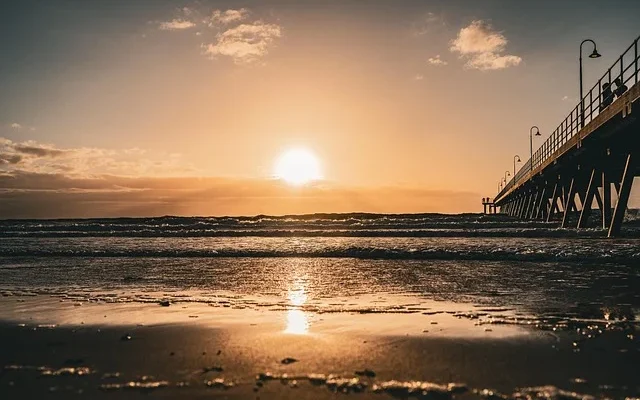 Sunset over a pier at Hermosa Beach, with the sun casting warm hues behind the structure.