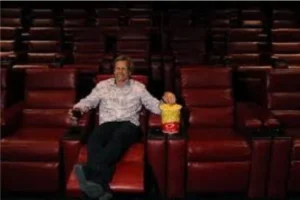 A man relaxes in a red recliner at the Reserved Luxury Recliners in Green Valley Theater, enjoying a movie.