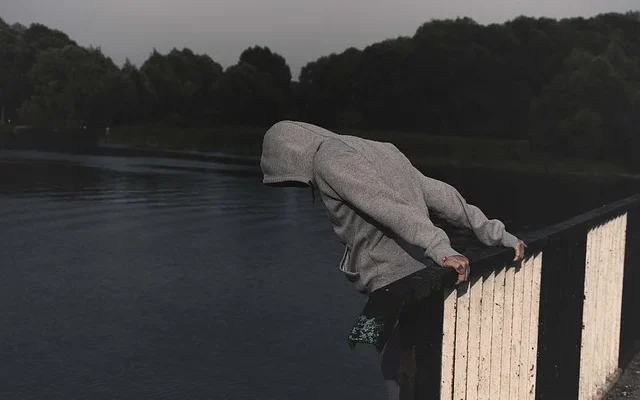 A hooded individual leans over a railing, with carrara luxury drug​ branding visible in the background.