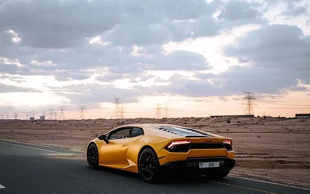 A sleek yellow sports car by make1m luxury cars​ maneuvering on a winding road with distant mountains in the background.