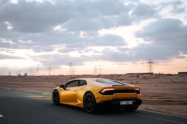 A sleek yellow sports car by make1m luxury cars​ maneuvering on a winding road with distant mountains in the background.