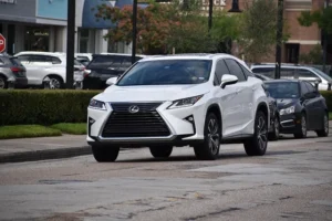 A white 2019 Lexus RX 350 driving down the street, showcasing luxury SUV features and style.