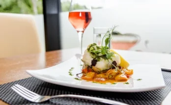 A white plate with gourmet food and a glass of rosé wine, set at Rose's Luxury D.C in Washington.