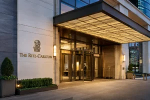 The Ritz-Carlton luxury hotel entrance with elegant architecture, warm lighting, glass doors, and landscaped surroundings at dusk.