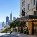 The Ritz-Carlton San Francisco luxury hotel entrance with San Francisco skyline, Transamerica Pyramid, bay, and cable car in the background.