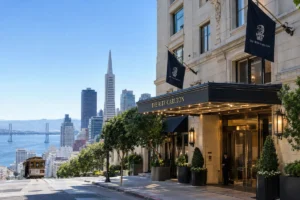 The Ritz-Carlton San Francisco luxury hotel entrance with San Francisco skyline, Transamerica Pyramid, bay, and cable car in the background.
