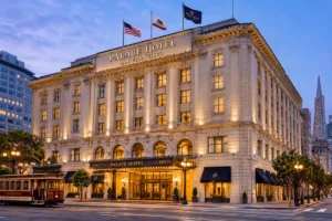 Palace Hotel San Francisco exterior at dusk, featuring its grand historic facade, illuminated entrance, and a classic San Francisco cable car in the foreground.