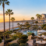 L'Auberge Del Mar luxury coastal hotel overlooking the Pacific Ocean with a swimming pool and palm trees in Del Mar, California.